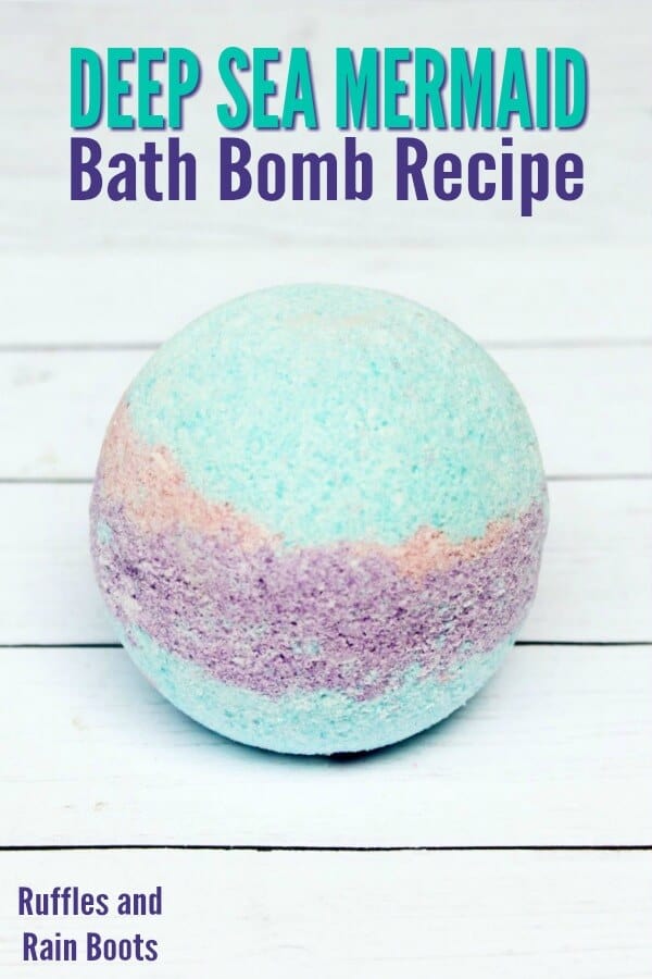 A close up image of a subdued, non-decorated mermaid bath bomb recipe showing the multiple colors used shown on a white wood background. 