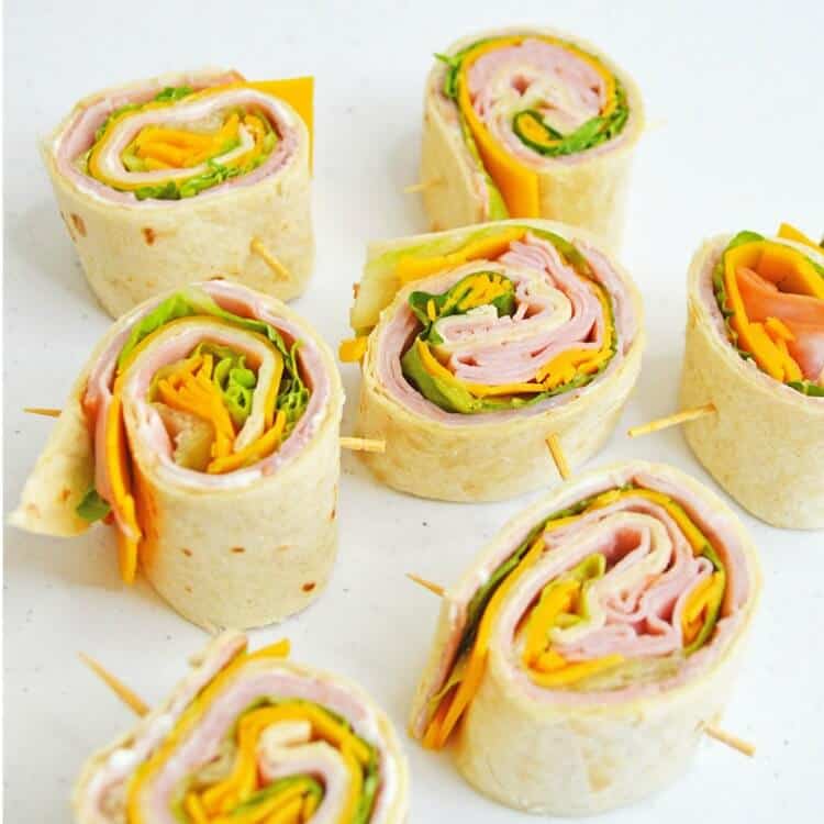 Ham and Cheese Pinwheel sandwiches rolled up in tortillas with picks on white plate.