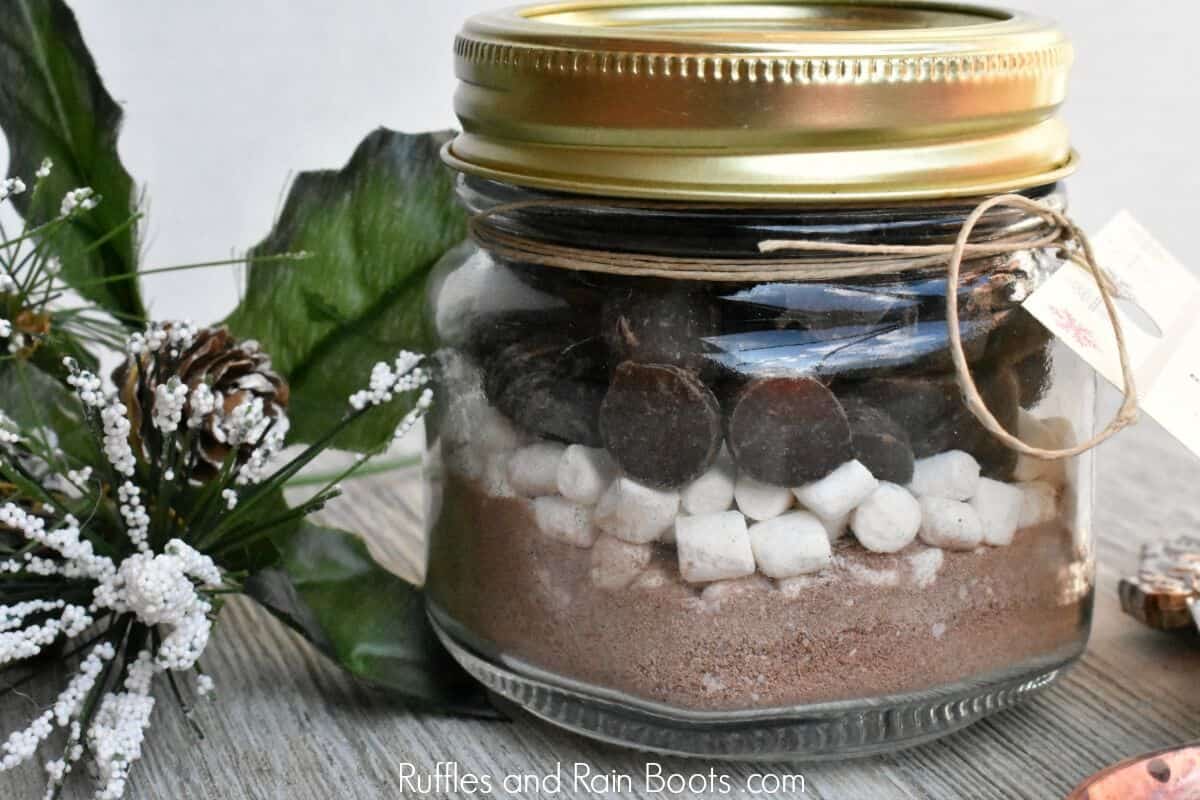 close up photo of mason jar hot cocoa gift with greenery on wooden table