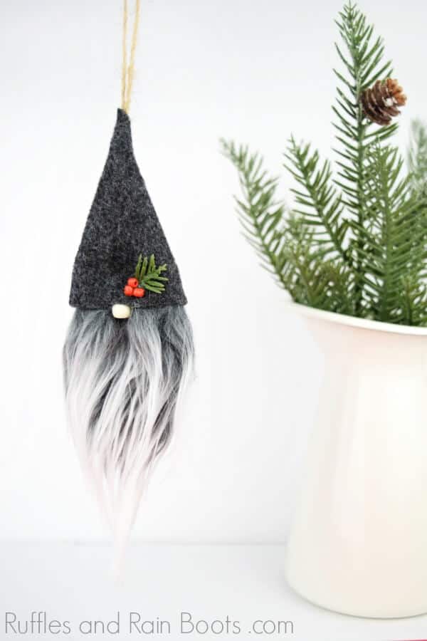 DIY Swedish Gnome Ornament with dark gray felt gnome hat hanging from a pine branch in a white pitcher.