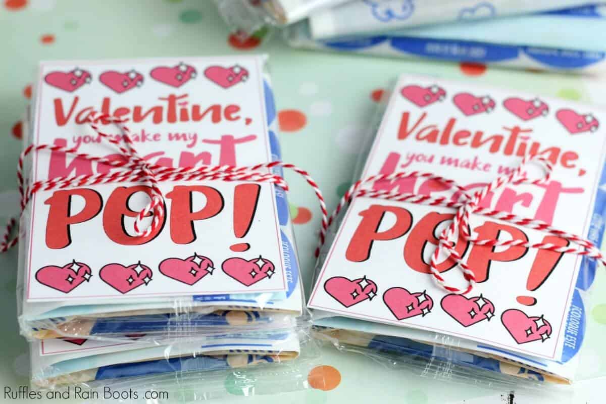 horizontal image of a stack of non candy Valentines Day classroom cards tied with red and white twine onto bags of microwave popcorn