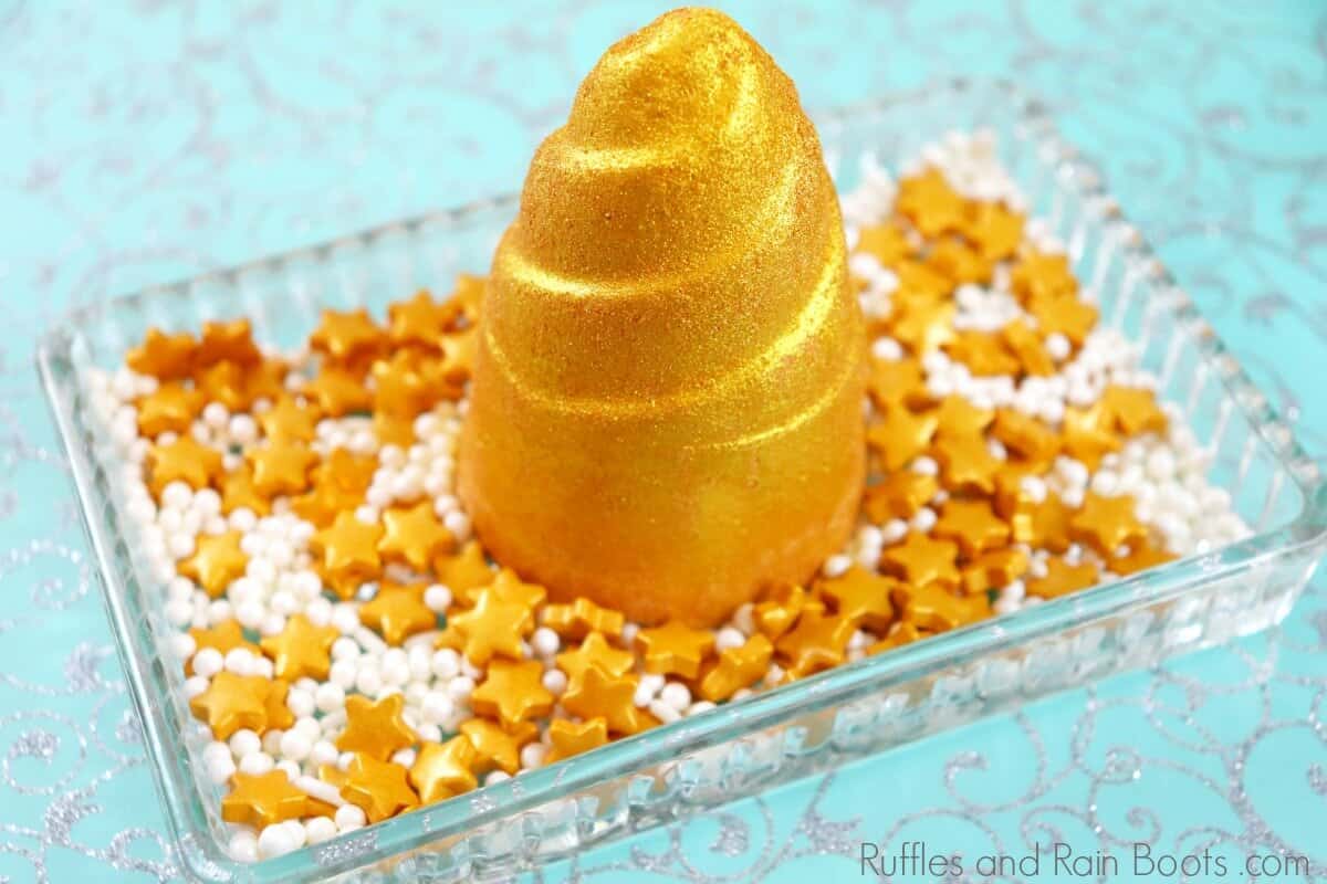 close up of gold DIY unicorn horn bath bombs sitting in a bowl of small gold stars and white balls with a blue background
