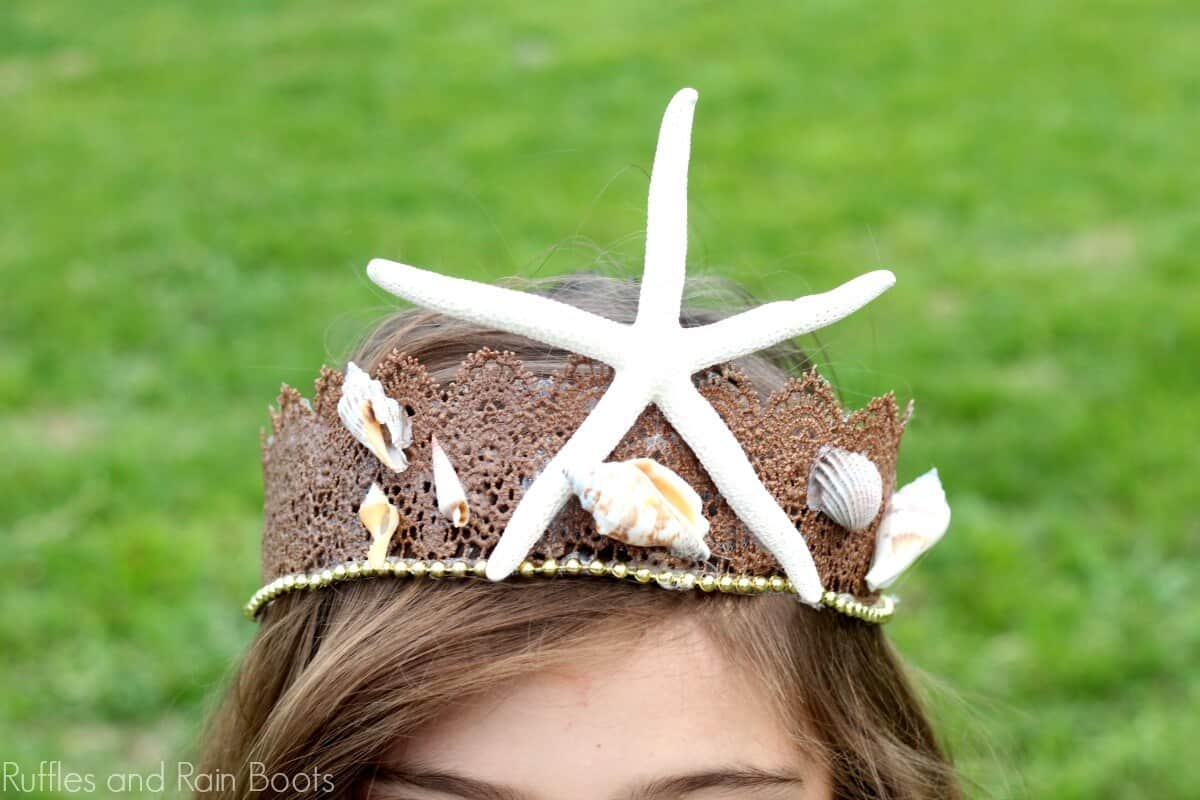 a little girl wearing a Mermaid Crown for Costumes or Dressup with a starfish and shells attached to it, while standing in a field of grass