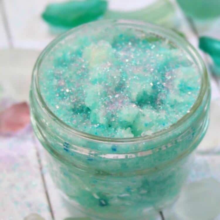 teal mermaid foot scrub in a clear jar on a white background surrounded by teal and green sea glass pieces