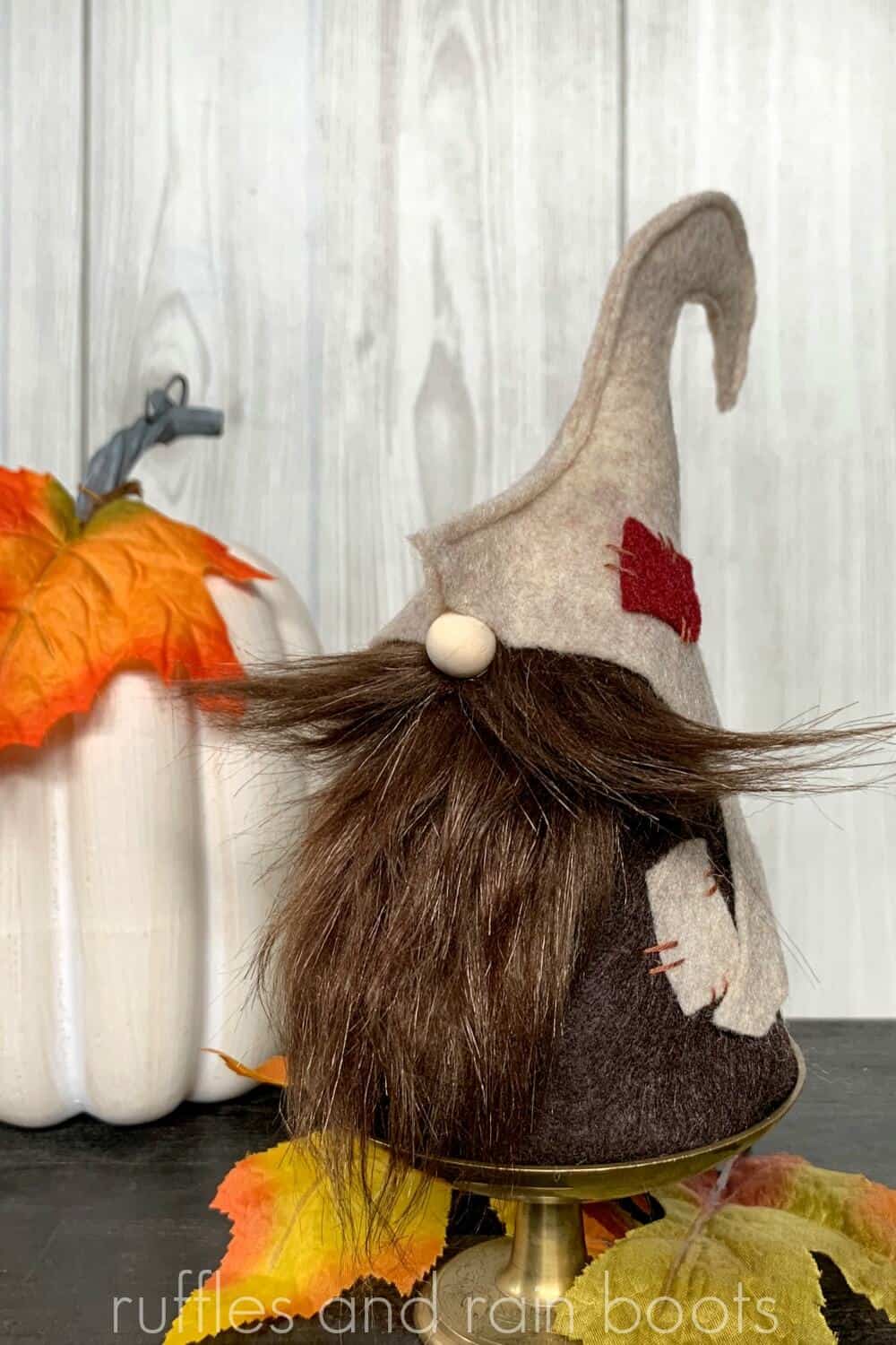 fall gnome made from felt and faux fur styled in front of a pumpkin with fall leaves on a wooden table with shiplap wall