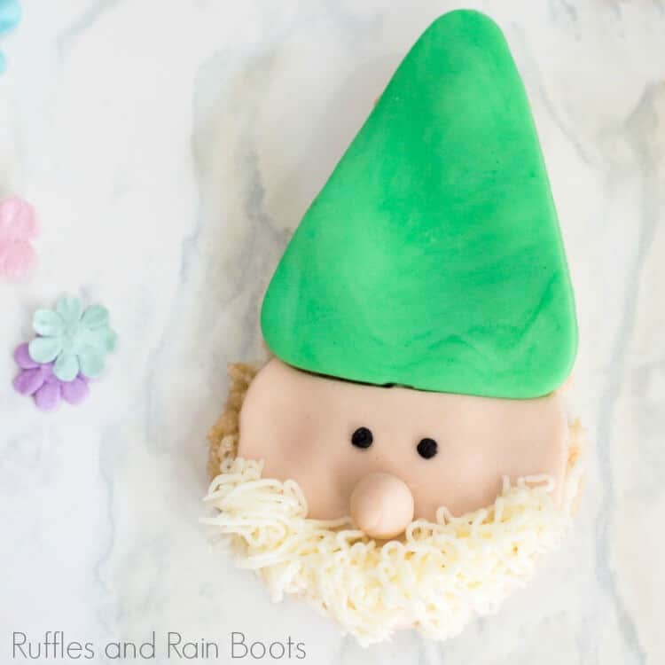 Close up square image of gnome rice krispies treats with green hat and frosting beard on a marble background.