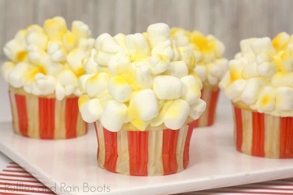 side view of popcorn cupcakes for circus party on a white cheese board on a red and white background