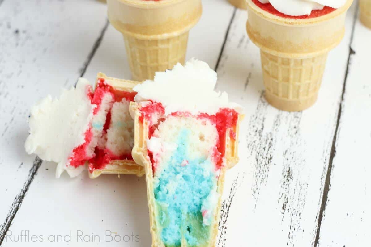 surprise patriotic ice cream cone cupcakes for 4th of july cut in half and laying on a wooden table with two additional ice cream cone cupcakes in the background