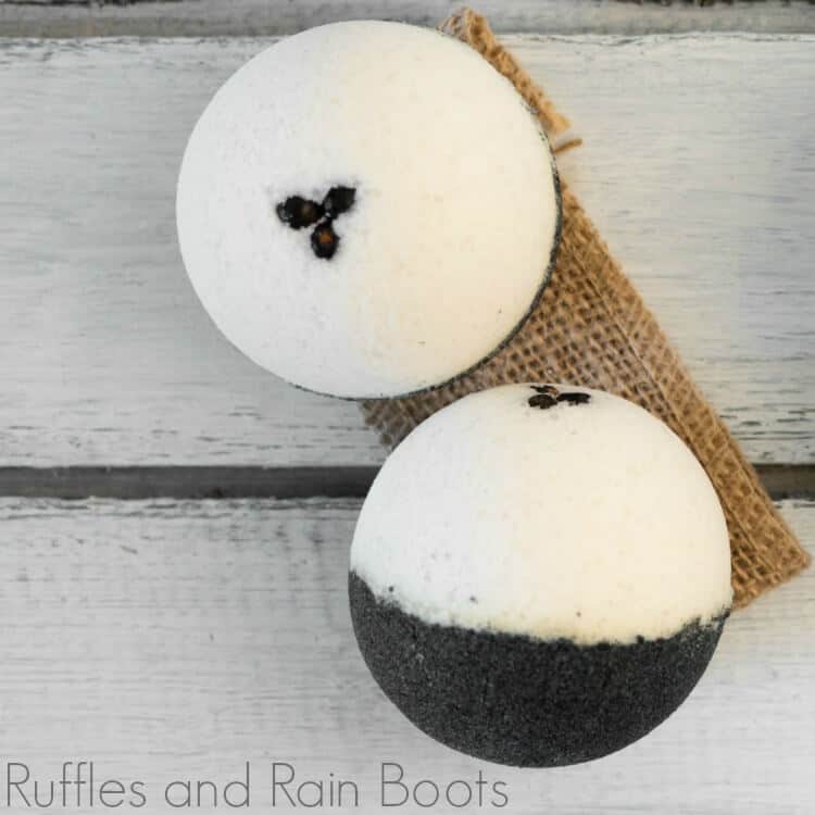 Overhead close up view of two coffee bath bombs in cream and brown on a brown burlap ribbon on a grey wood table.