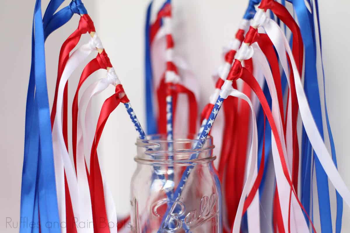 Diy ribbon wands made in red, white, and blue with starred sticks in a mason jar on a white background.