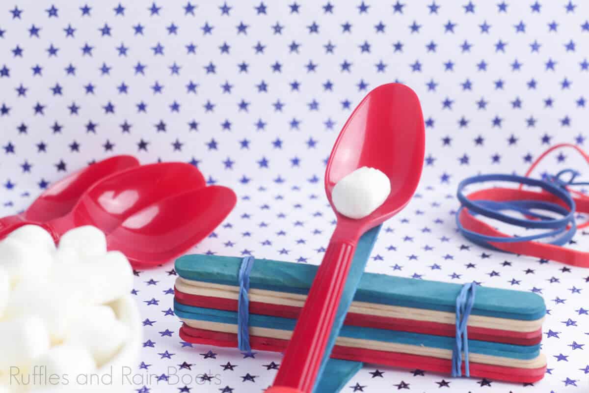 marshmallow catapults for kid science projects with spoons and popsicle sticks with marshmallows on a blue and white polka dot background