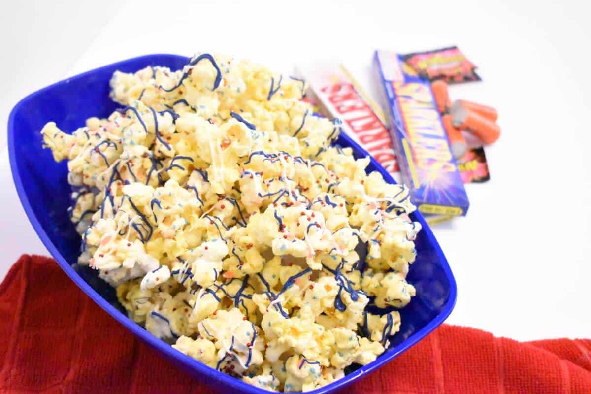 july 4th popcorn with red white and blue candy and pop rocks on white table with firecrackers