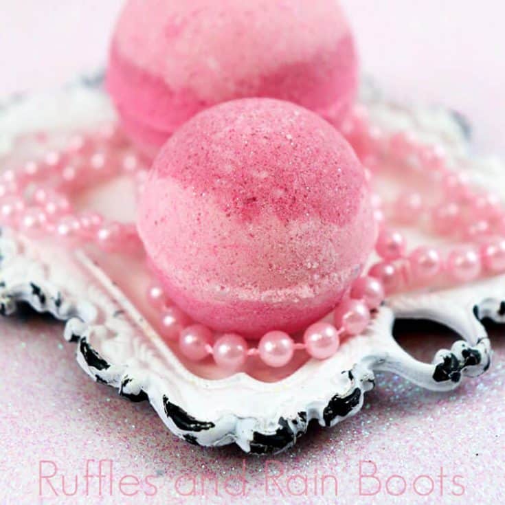 two pink striped princess aurora bath bombs on a white antique square plate with toy pink beads on a pink table