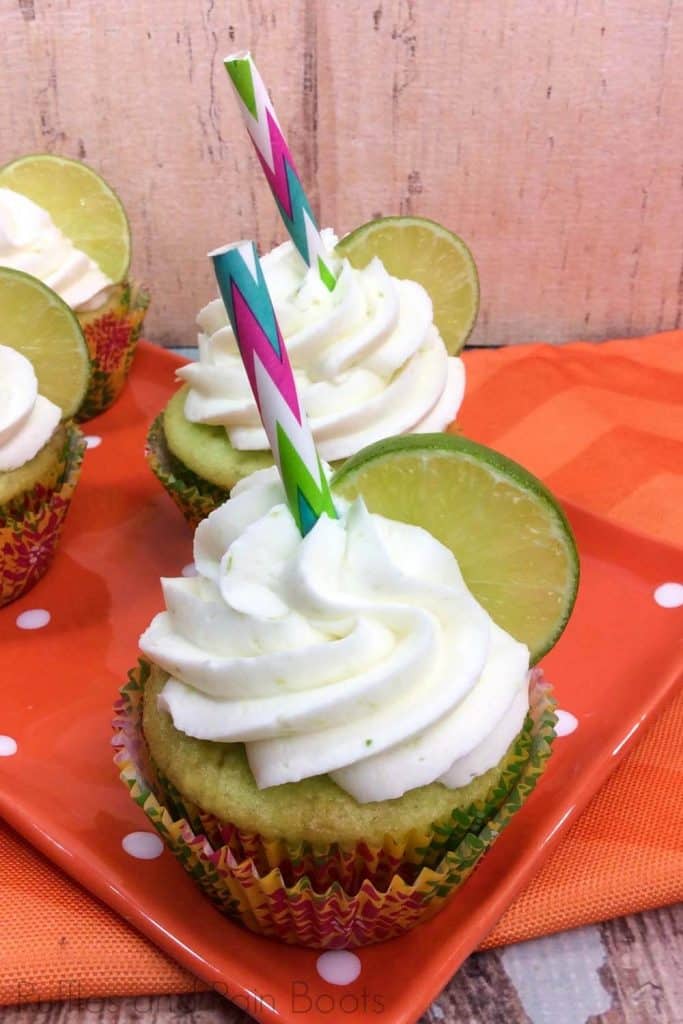four key lime cupcake ideas with a lime on top of white icing on a wood table with an orange linen