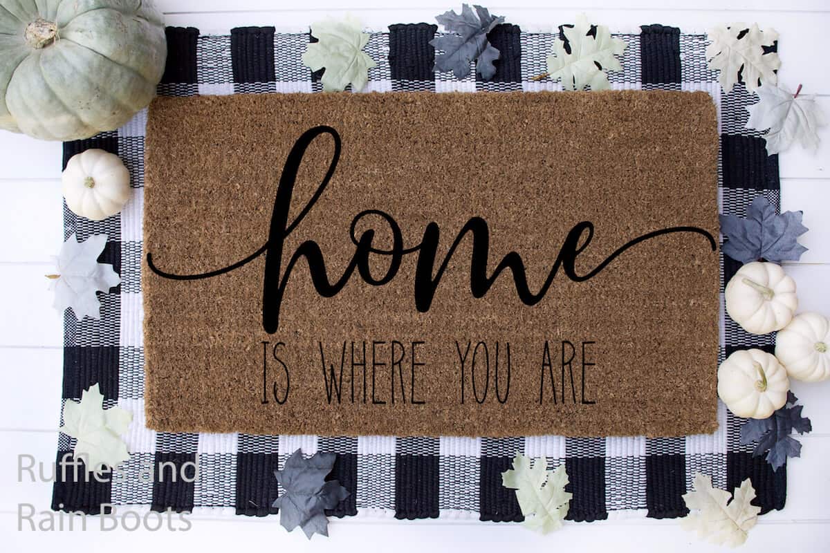 home is where you are Farmhouse SVG for cutting machines on doormat on a buffalo check mat on a white wood background