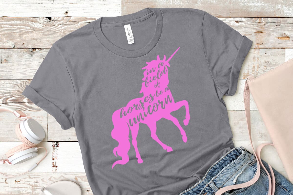 in a field of horses be a unicorn cut file for cutting machines on grey t-shirt with jeans and headphones on a beige wood background