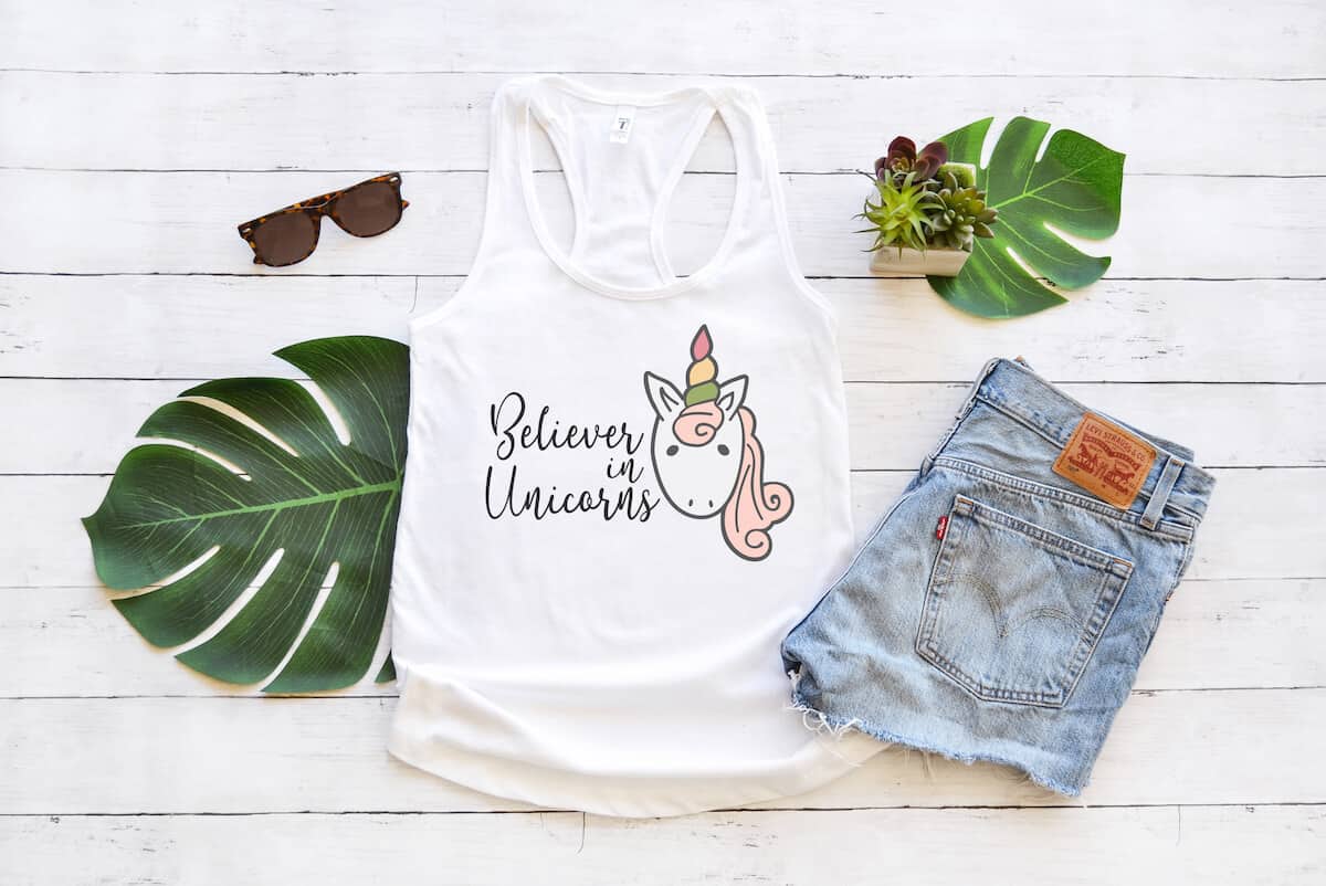 Believer in Unicorns free unicorn svg on tank top with jean shorts and palm leaves on a white wood background