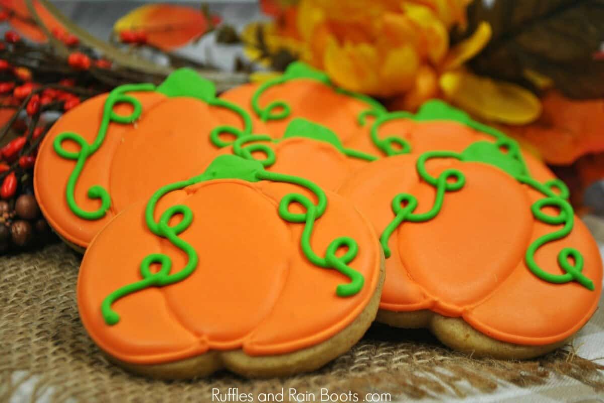 front view of a stack of pumpkin spice cookies with orange royal icing with green pumpkin leaf tendrils on a fall background 