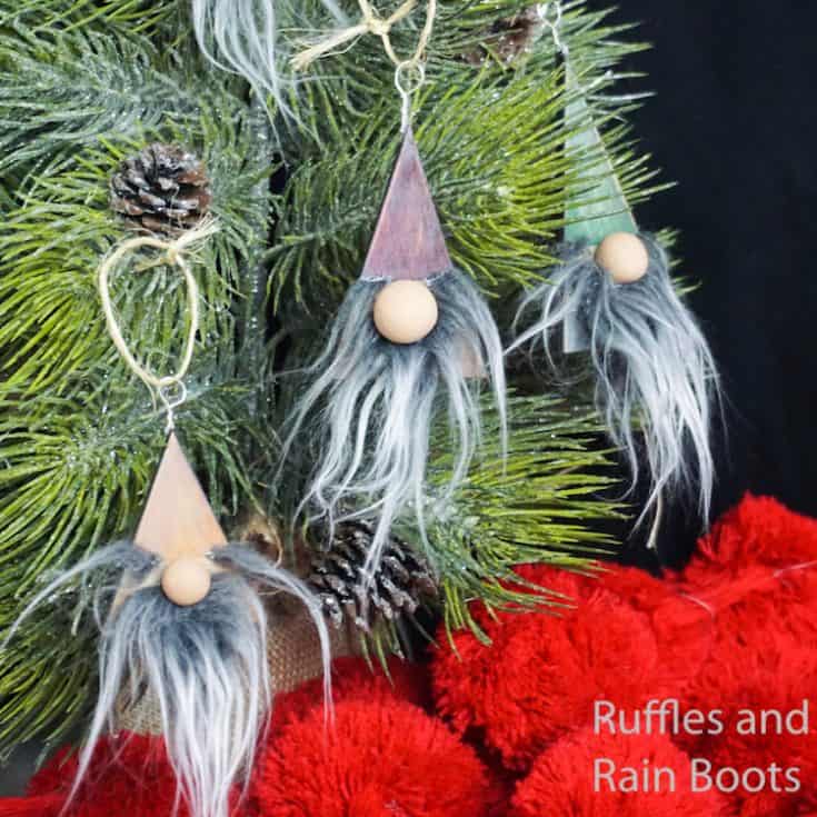 easy wood ornament gnomes hanging on a christmas tree in front of a black background
