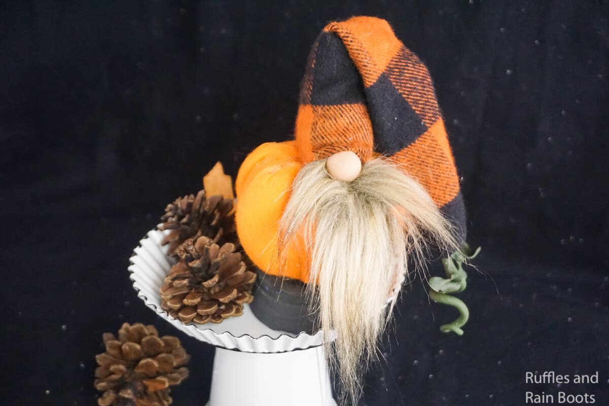 how to make a fall gnome with a pumpkin shape on a white cupcake stand with pinecones on a black background