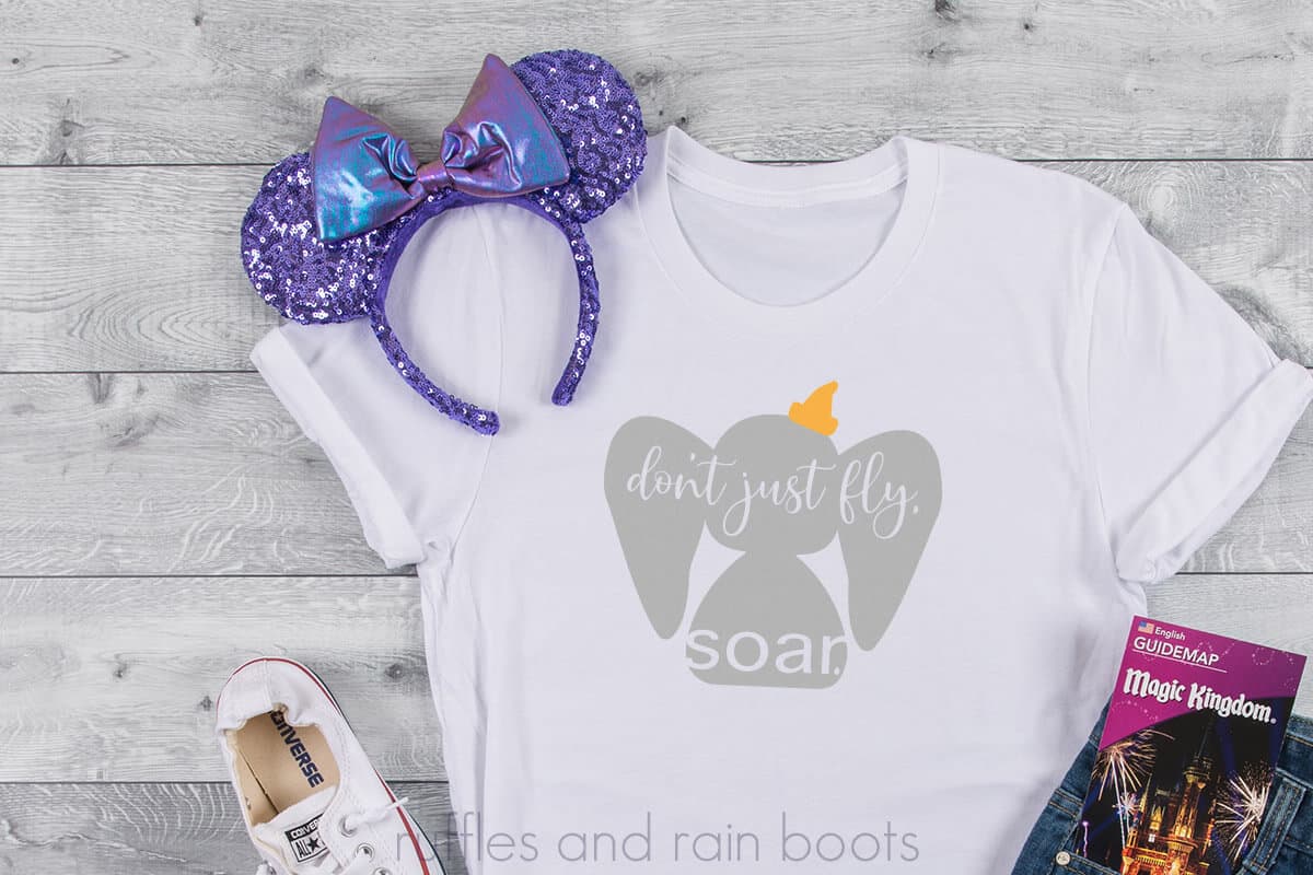 Disney Dumbo SVG in gray with yellow hat placed onto a t-shirt with a vinyl Cricut project idea with text which reads dont just fly Soar