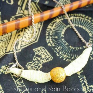 Golden Snitch Necklace Clay on a black background with a wand