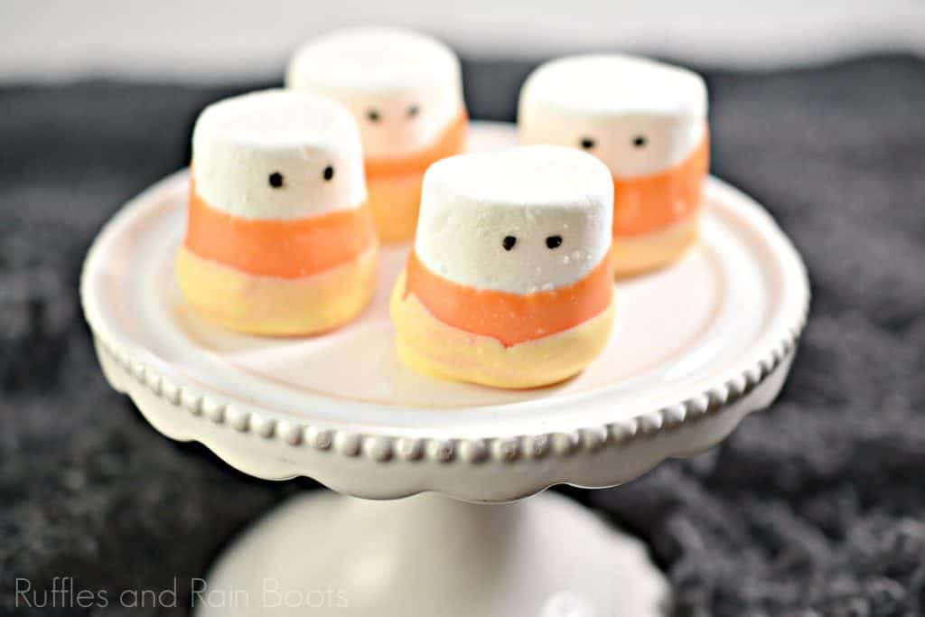 Candy Corn Dipped Marshmallows for Halloween on a white cupcake platter on a black background