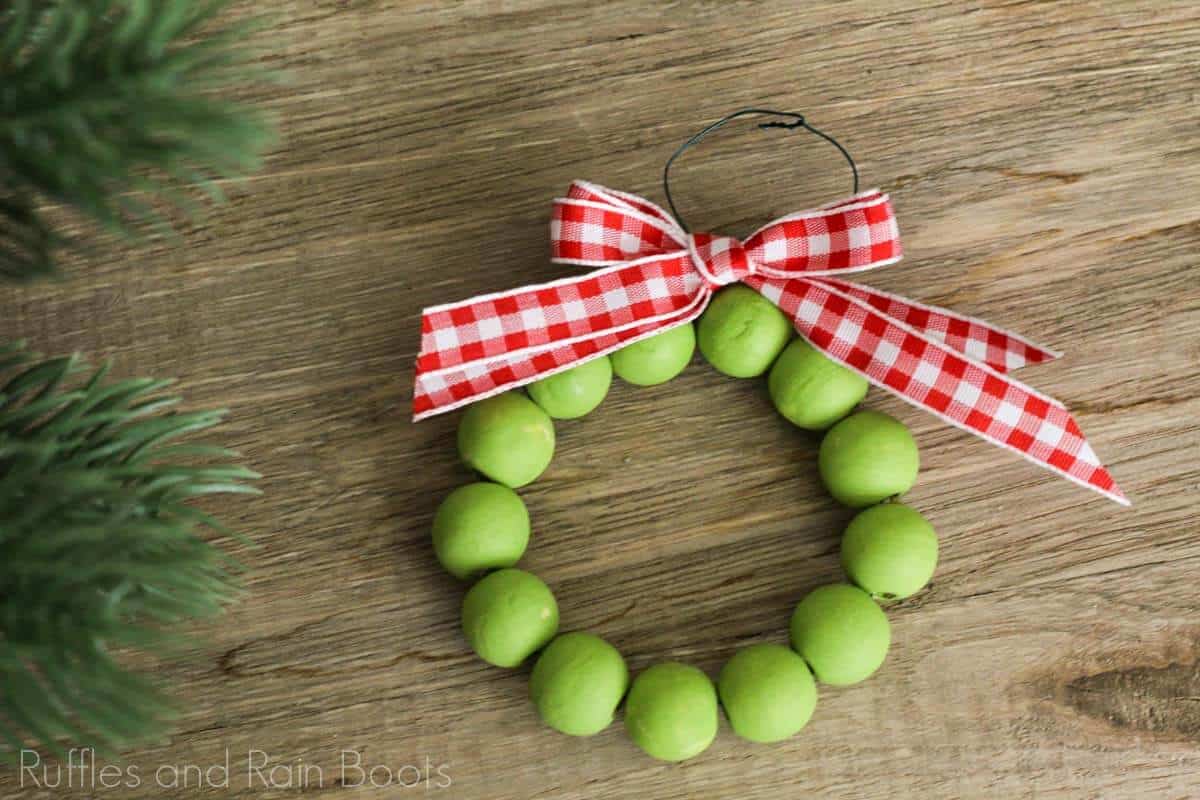 Horizontal image of a Christmas ornament idea for rustic wood bead wreath on a wood table with a red gingham check ribbon bow.