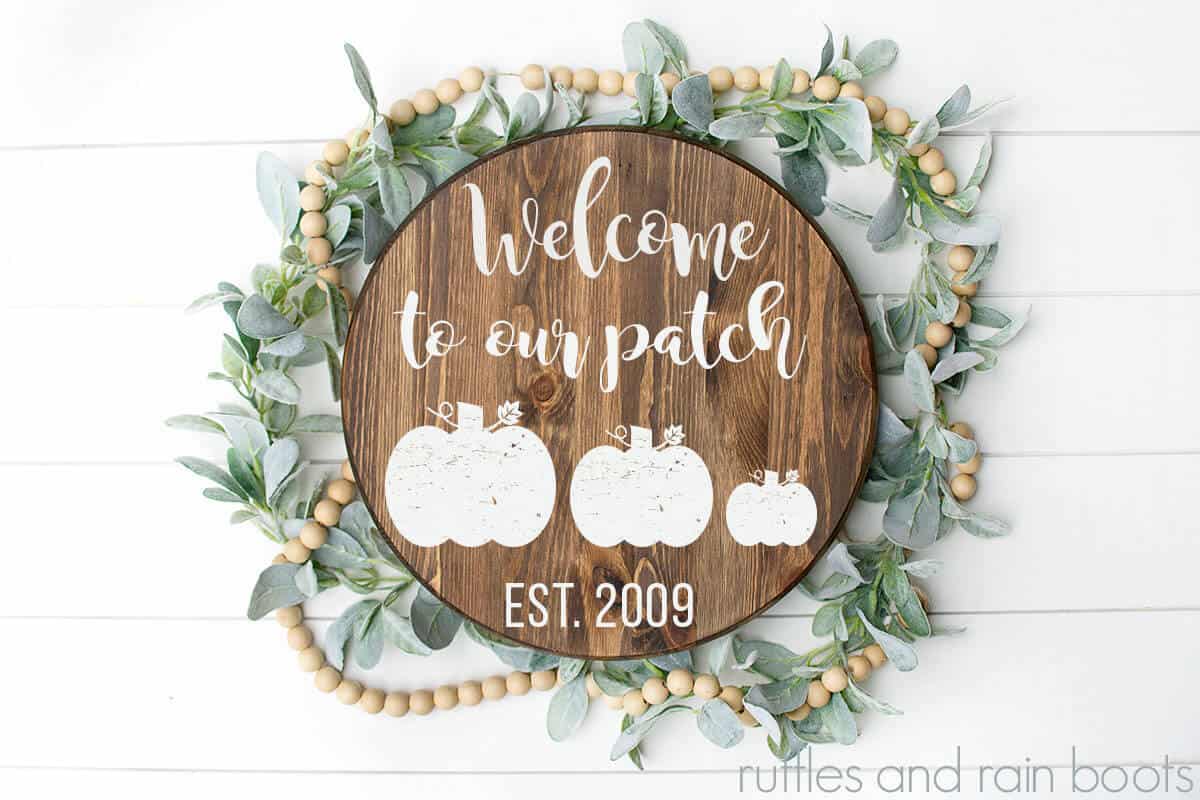Welcome to Our Patch Pumpkin Cut Files for Free on a wood round sign with some fall floral and wooden beads on a white background