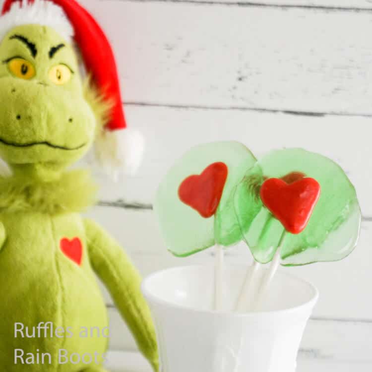 how to make homemade lollipops that are grinch themed on a white wood background with a grinch toy