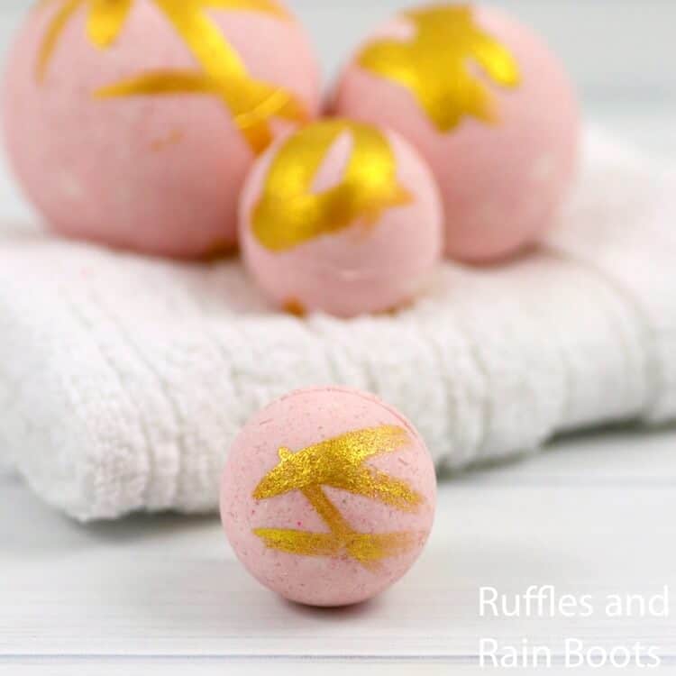 Four pink and gold bath bombs on white towel on white wood background.
