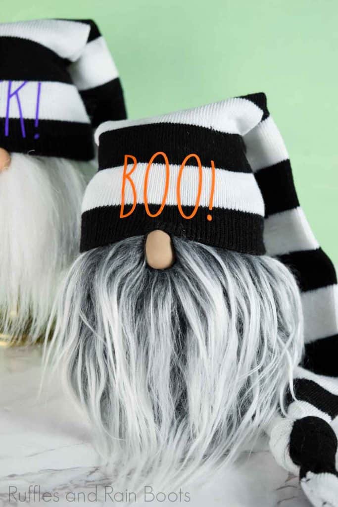 Halloween sock gnome with gray and white faux fur beard and striped hat which reads Boo on a green background.