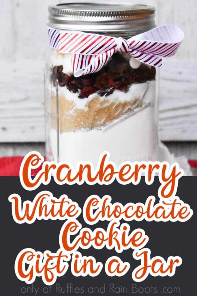 side view of jar filled with cookie ingredients with text which reads Cranberry White Chocolate Cookie gift in a jar