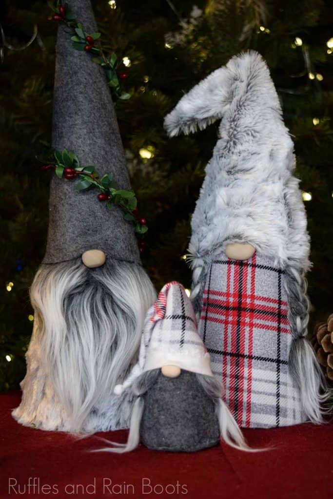 Vertical image of a set of three Christmas gnomes in a family made with the cone gnome tutorial on lush table and Christmas tree background.