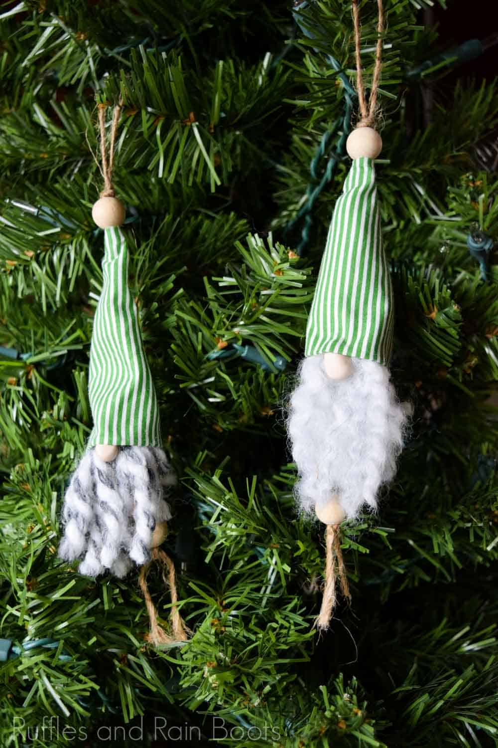 Vertical image showing two gnome ornaments with yarn beards with green striped hats and wood bead noses hung on a small Christmas tree.