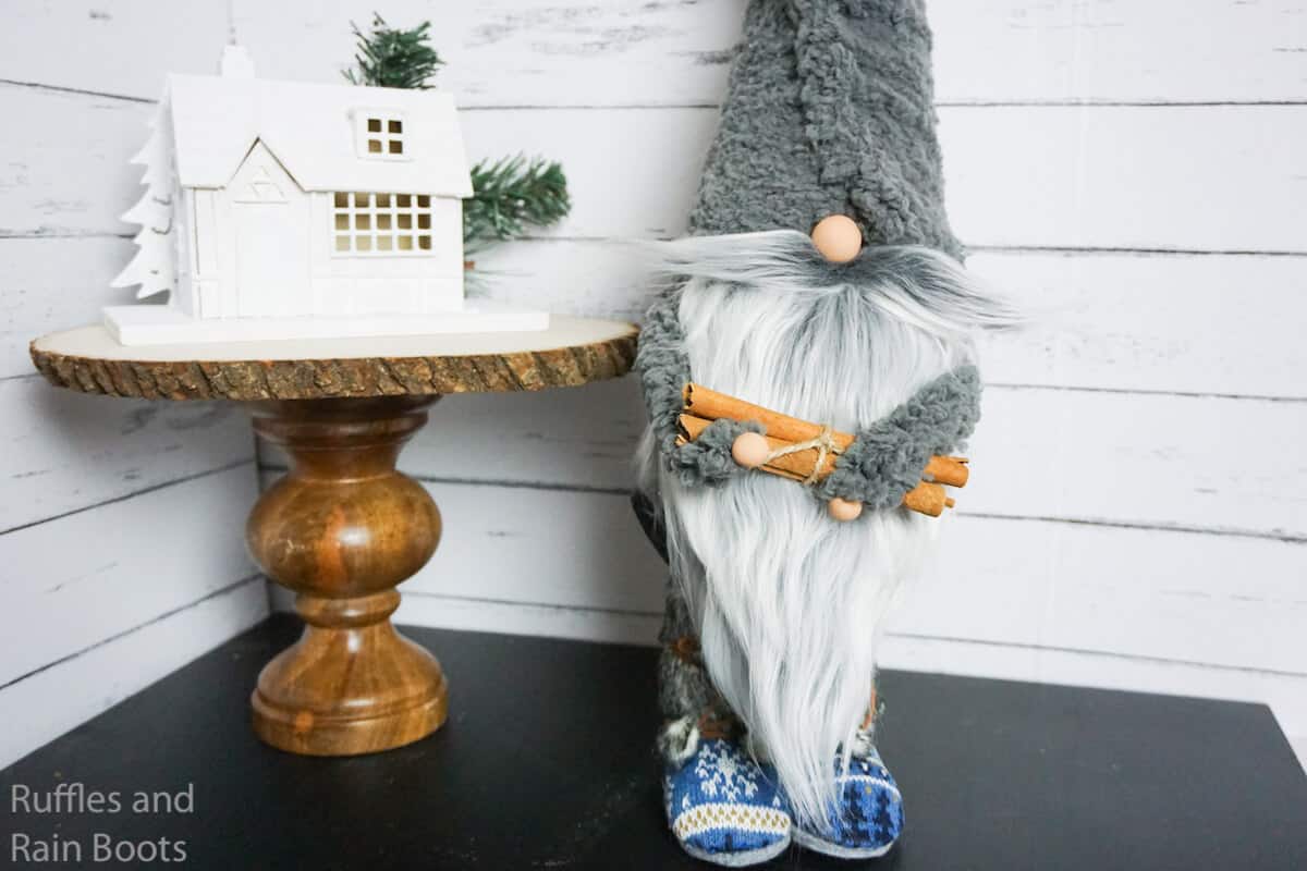 Horizontal image of a gray hat gnome with large gnome beard holding cinnamon stick firewood wearing gnome boots. 