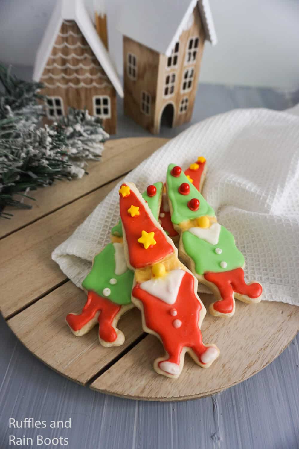 Close up image of elf-shaped gnome cookies on a holiday background with gingerbread houses.