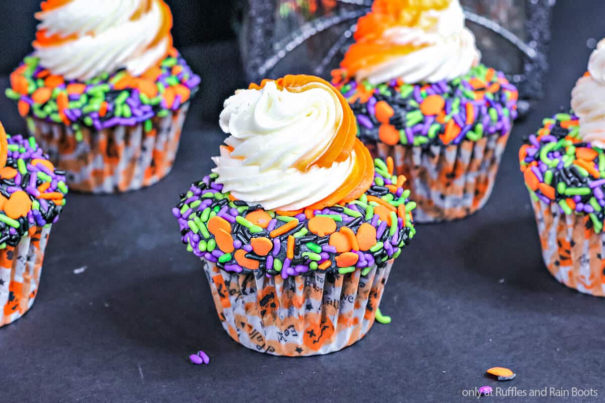 Horizontal image of an easy decorating idea for Halloween cupcakes with orange and white swirled frosting and a sprinkle shelf on a black background.