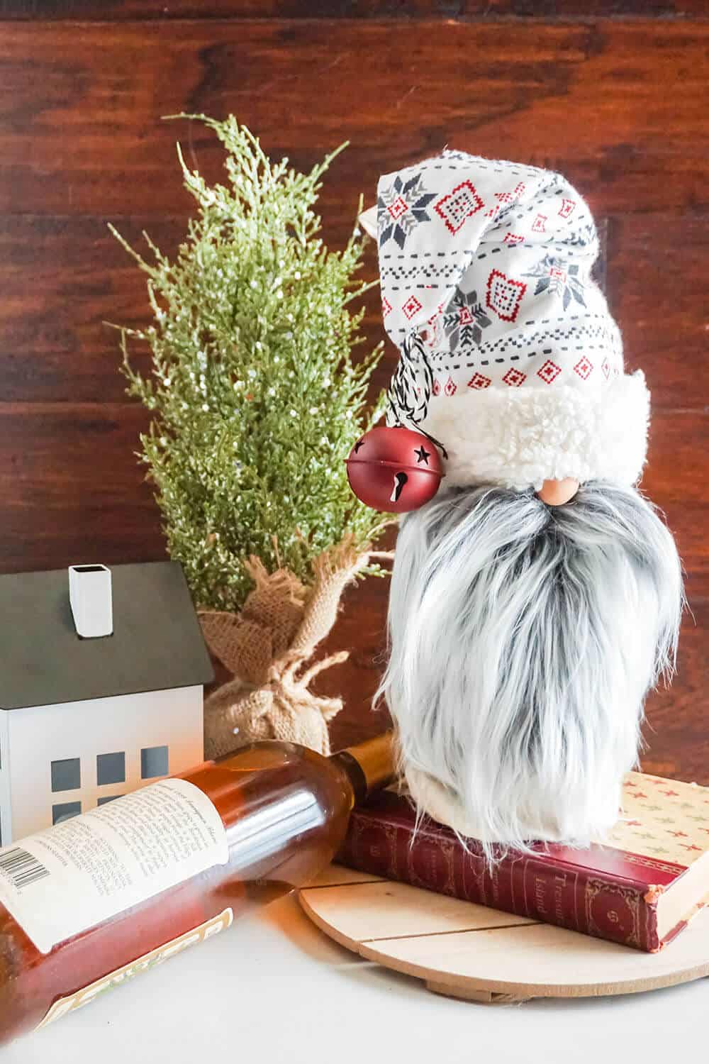 Close up image of a gnome bottle topper gift bag in front of a holiday background with a wine bottle.