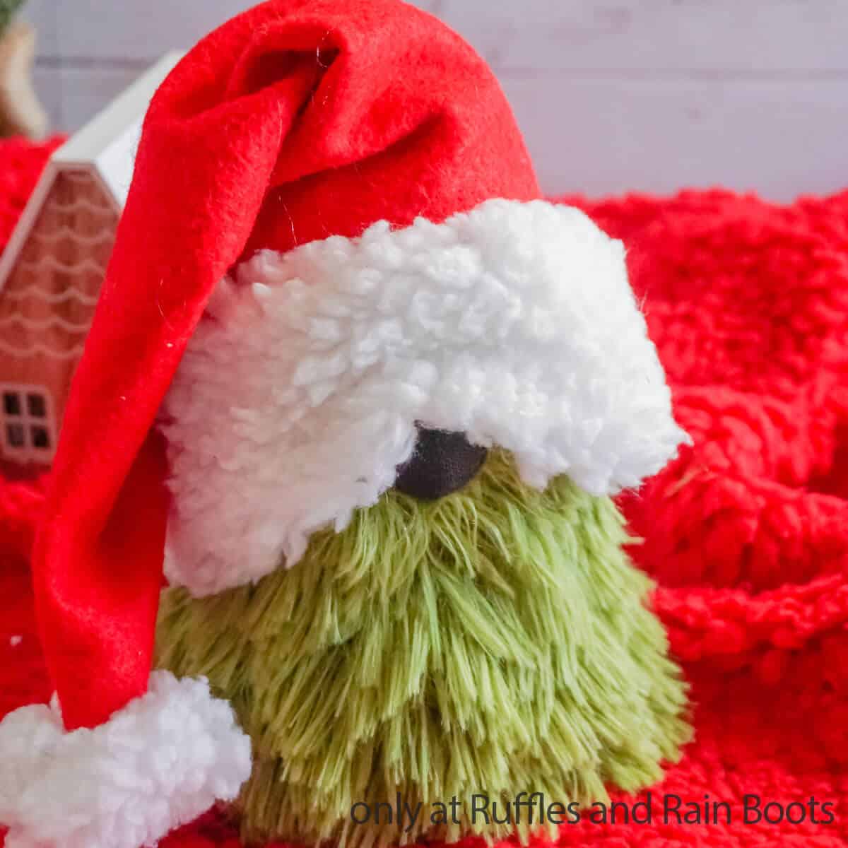 square image of a close up view of the Dollar Tree grinch sock gnome made with a pillow, felt, and a black sock on a red and white Christmas background with text which reads only at ruffles and rain boots