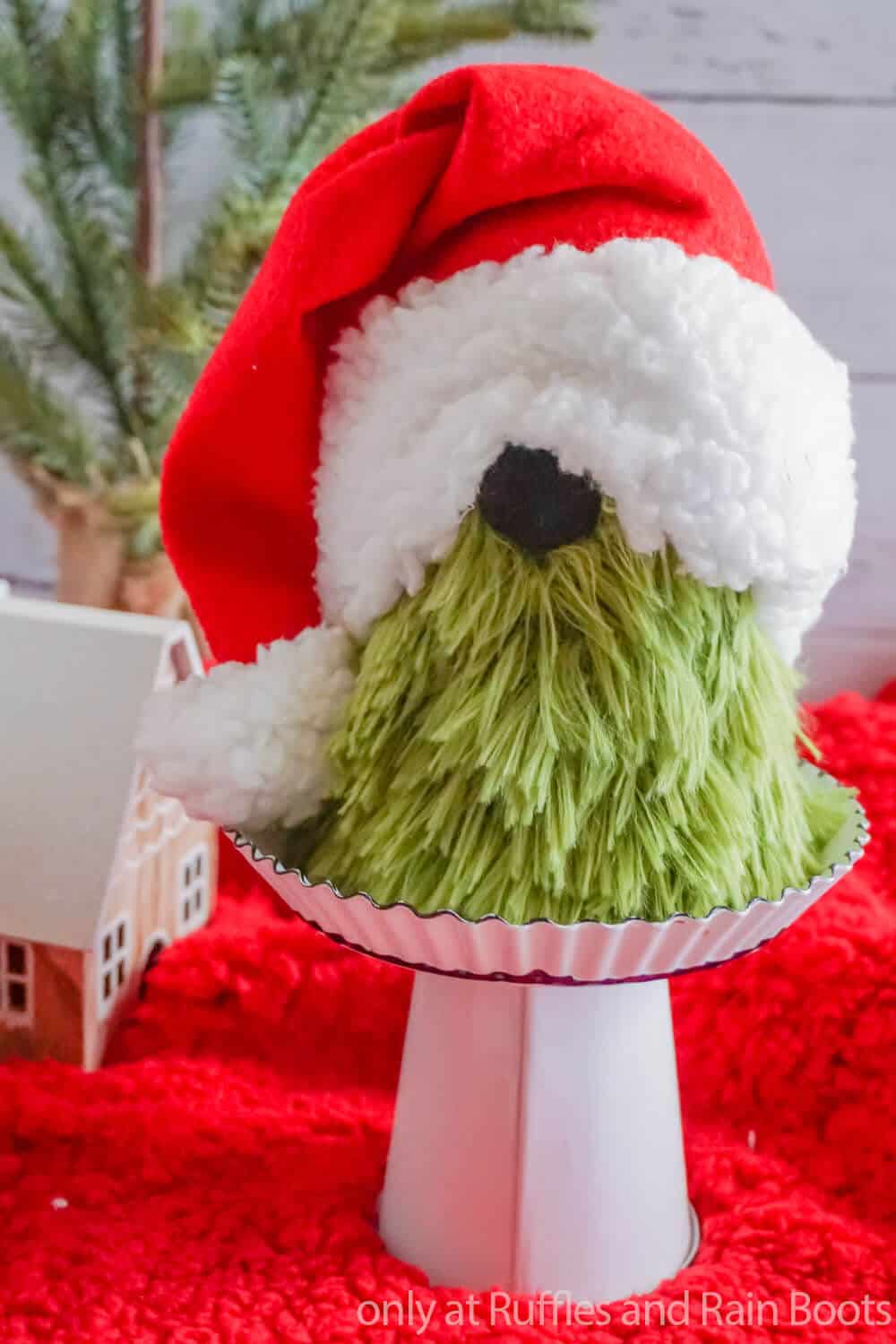 close up of dollar tree grinch gnome from a sock with a green beard, black nose, and red hat with white fluffy trim on a holiday background