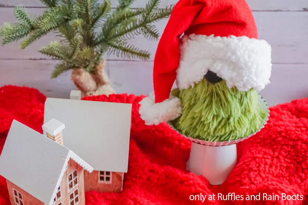 a green white and red dollar tree grinch sock gnome on a silver pedestal in front of Christmas background