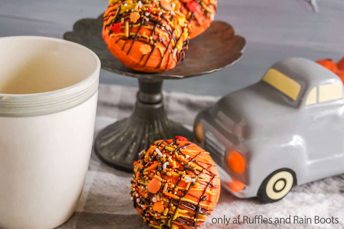 Photo of pumpkin spice hot cocoa bombs on a raised tray with a mug.