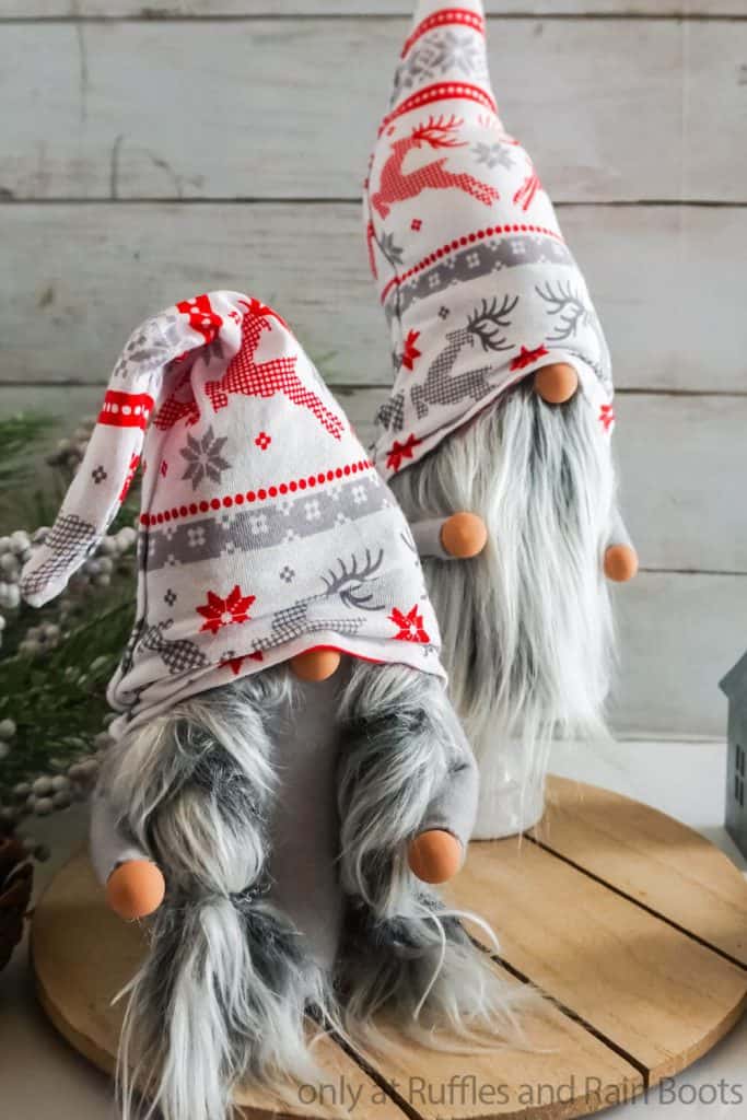 Vertical image of traditional Scandinavian boy and girl Christmas gnomes on wood round in front of holiday background. 