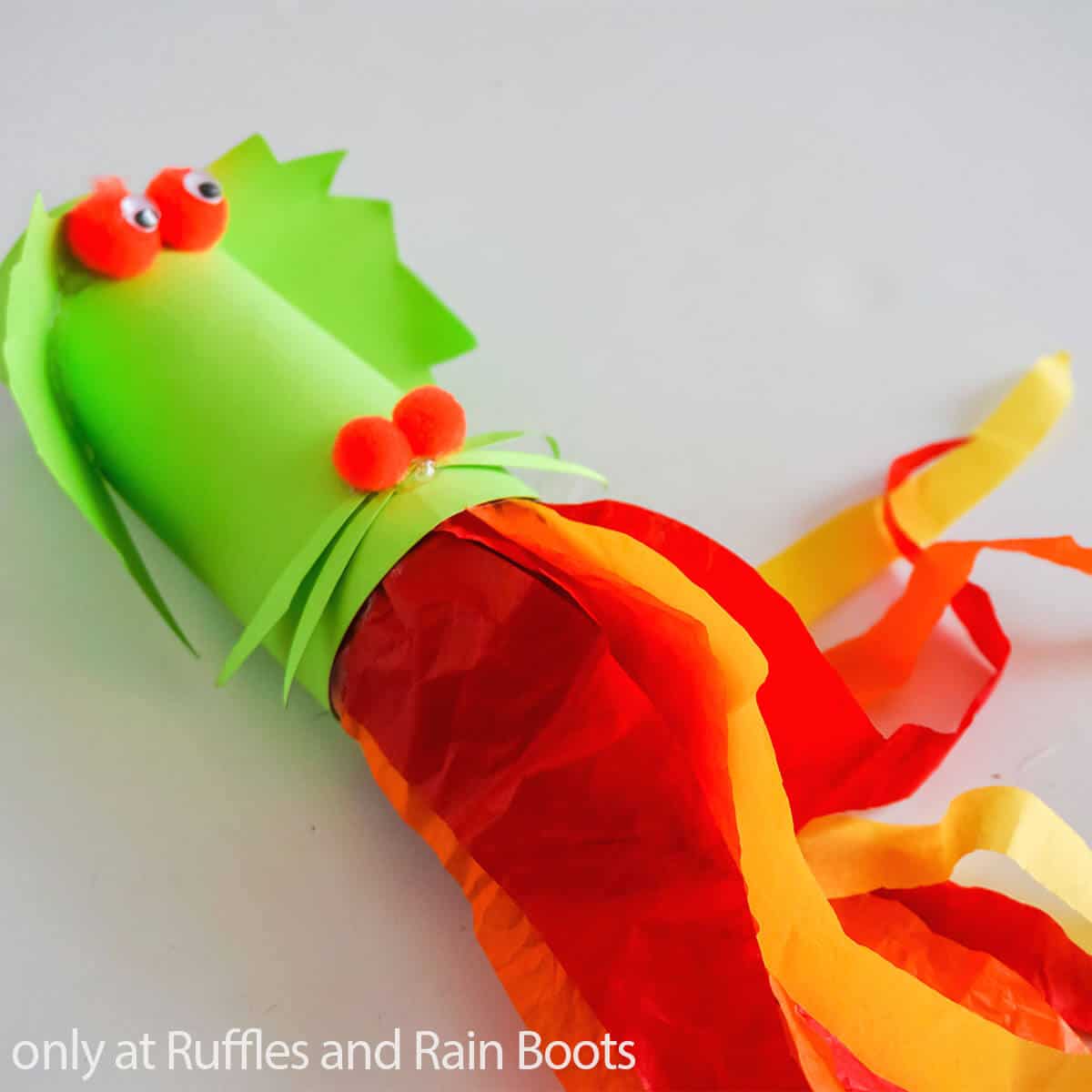 A green, red, orange, and yellow dragon blower paper craft for kids on a white background.