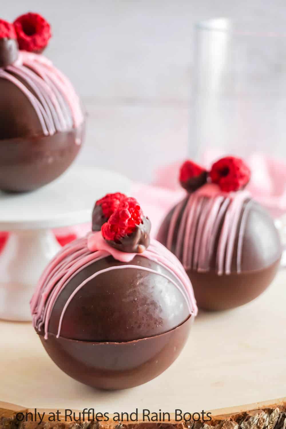 Raspberry and dark chocolate DIY hot cocoa bombs on wood round.