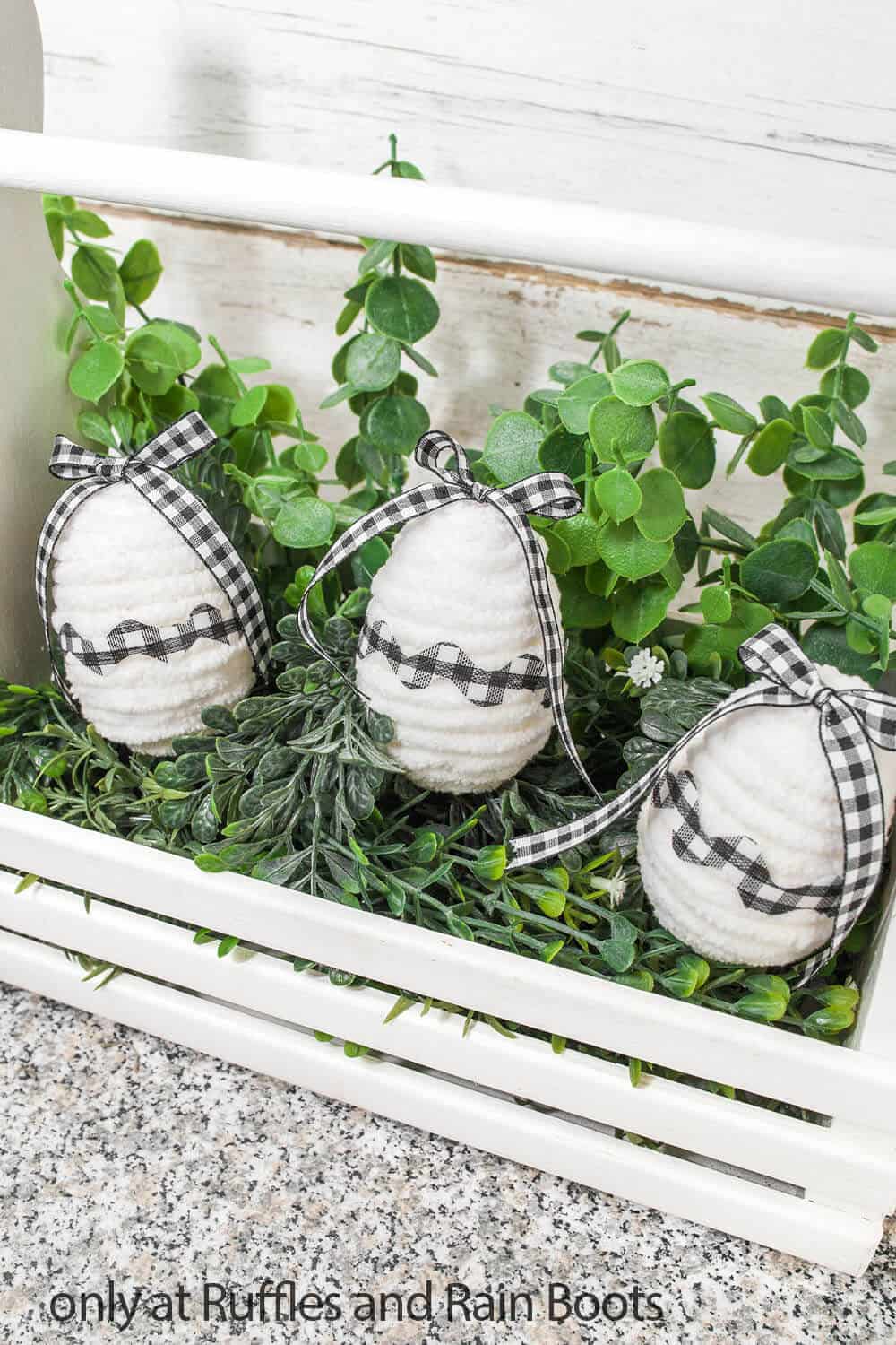 Close up image of DIY farmhouse Buffalo plaid easter eggs placed on greenery in a white wood miniature tool box.