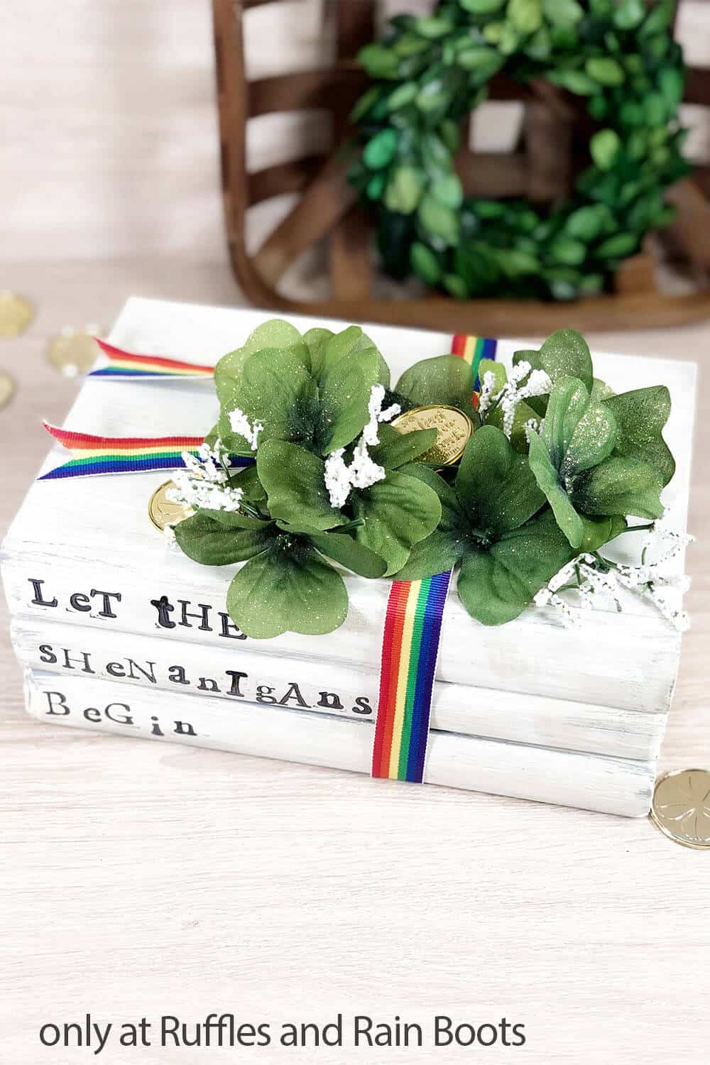 Farmhouse St Patrick's day book stack in white with rainbow ribbon, Dollar Tree clover greenery, and gold coins with let the shenanigans begin in stamped black ink.