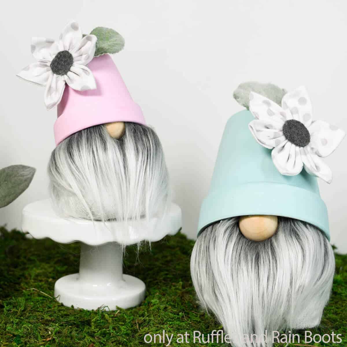 Two DIY Spring gnomes with a flower pot hat, fabric flower, and faux greenery on a bed of moss.