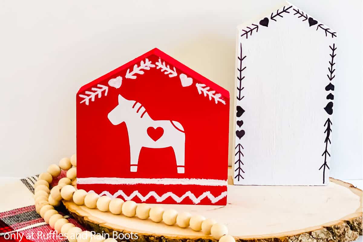 Horizontal image of two wood houses on a rustic table painted with simple Scandinavian accents and a Dala horse.